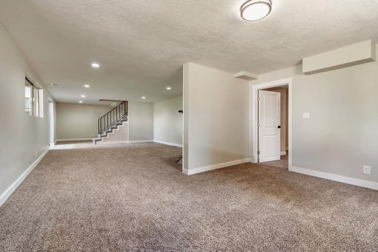 Finished basement with open living area, carpet, recessed lighting, and view of stairs leading up — Utah basement finish by CasaMás Construction