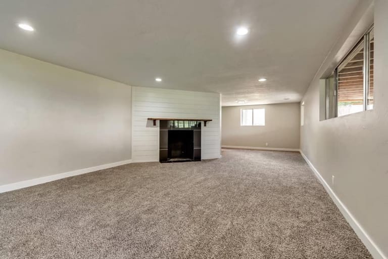 Finished basement family room with white shiplap accent wall framing the fireplace, recessed lighting, carpet, and basement-height windows — Utah basement finish by CasaMás Construction