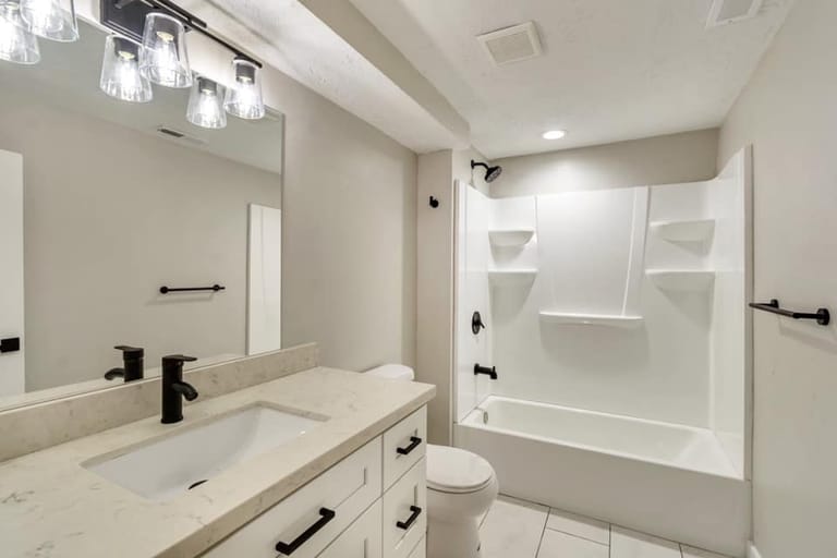 Bathroom with modern glass globe light fixture, single vanity, white tub-shower combo, and black hardware — Utah bathroom by CasaMás Construction