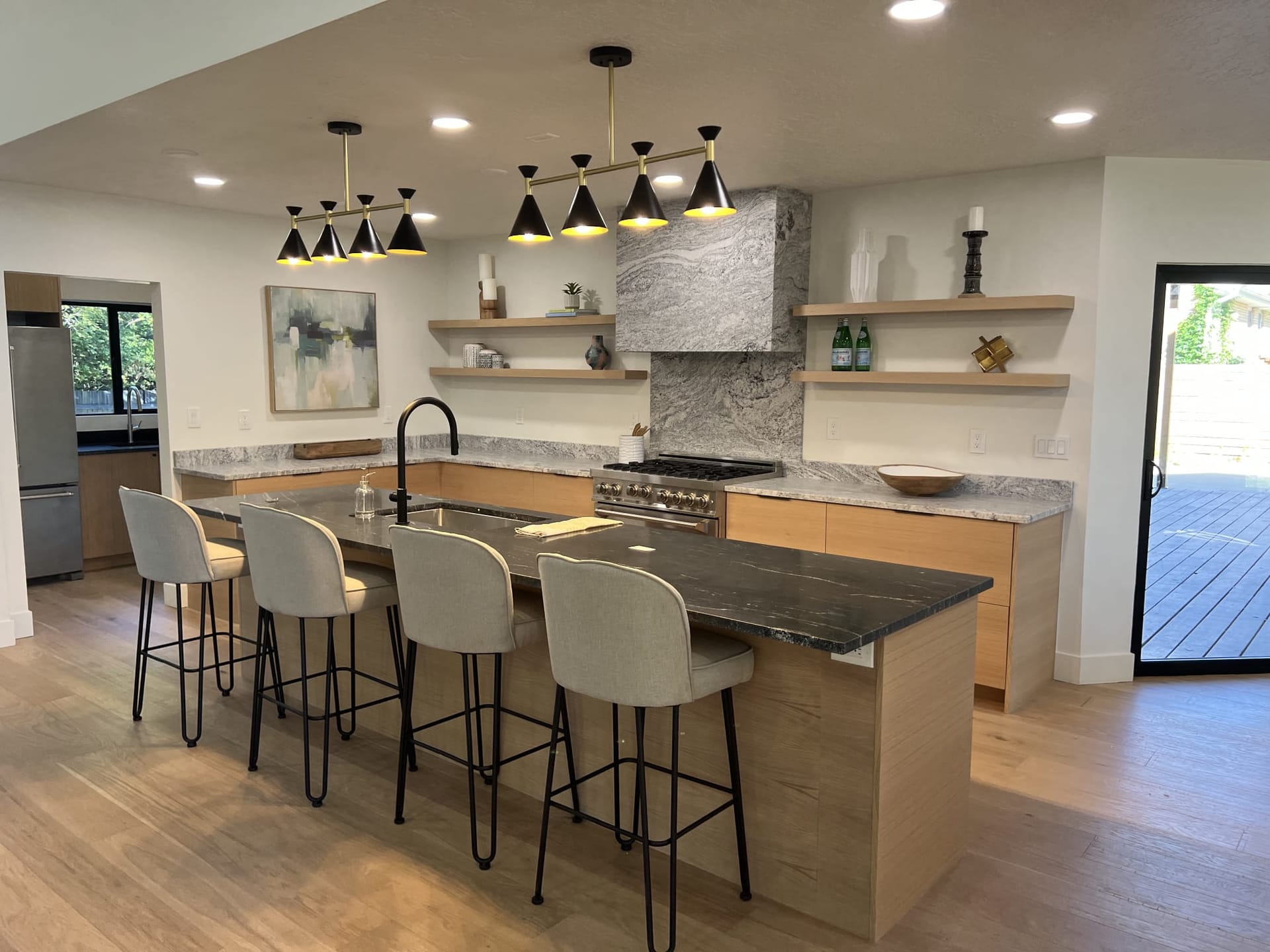 Luxury kitchen with black-and-brass cone pendant lighting, stone waterfall island, light-wood lower cabinets, and floating shelves — Utah kitchen addition by CasaMás Construction