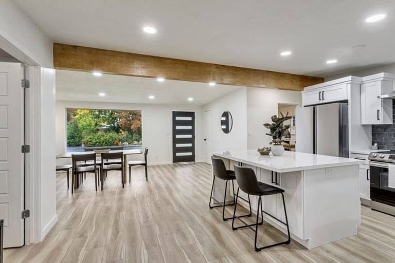 Open-plan kitchen and dining room with exposed wood beam, white cabinetry, central island, and stainless appliances — Utah kitchen and dining addition by CasaMás Construction